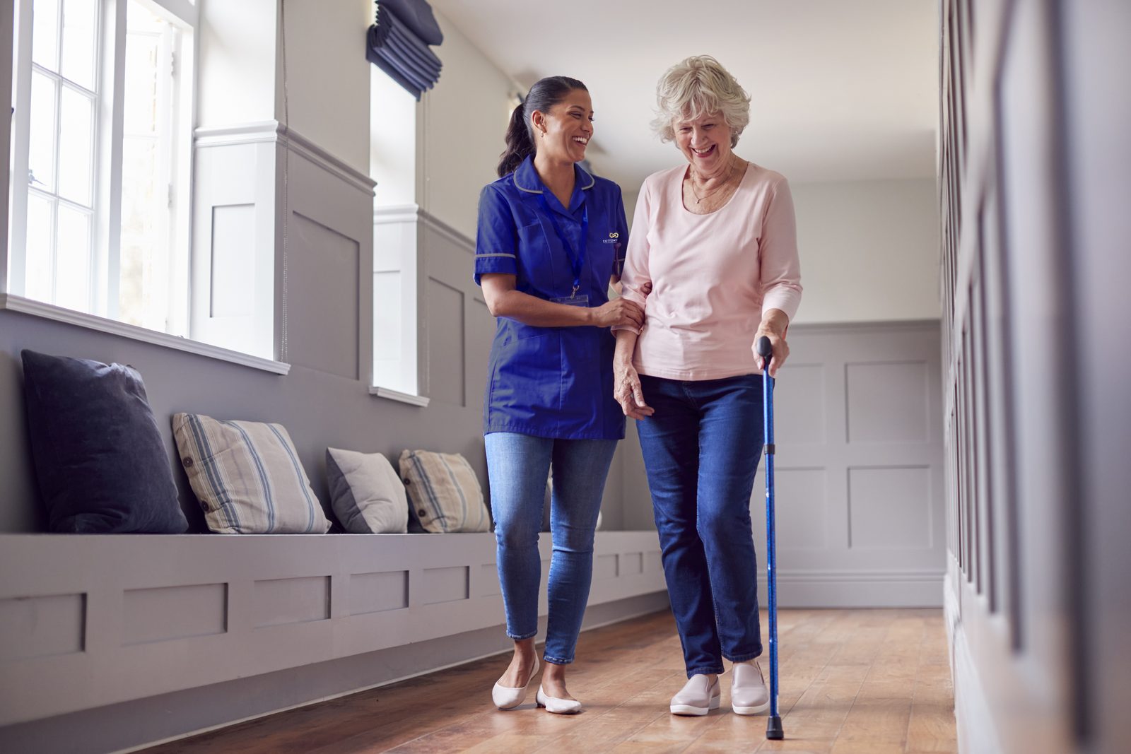 A nurse walking arm in arm with a resident down a bright hallway